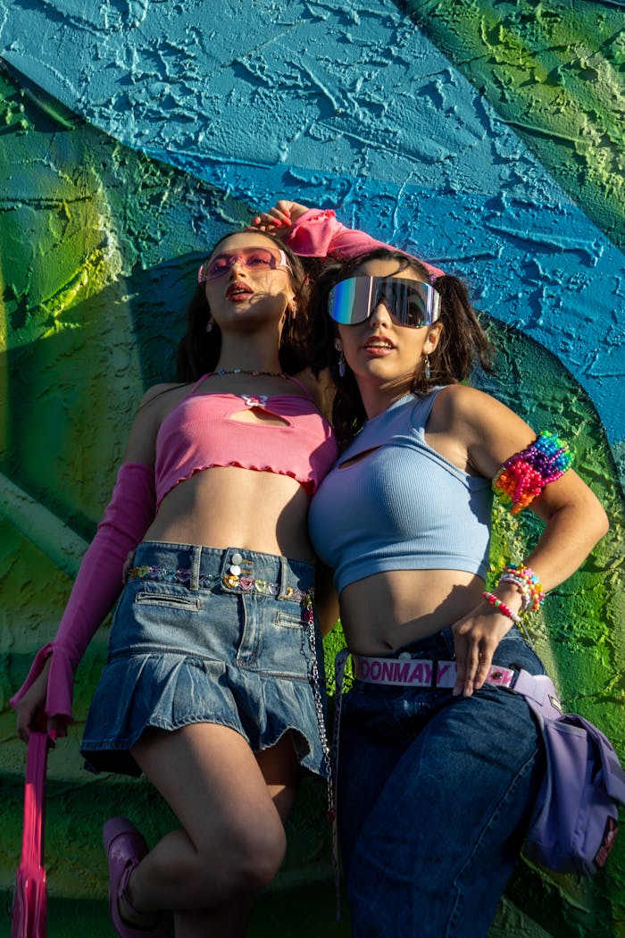 Two fashionable young women in vibrant outfits pose against a colorful graffiti wall, exuding confidence and style.